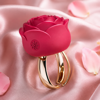 A rose-shaped intimate massager with a glossy pink silicone flower head and a polished gold-tone metal base, displayed on draped pink satin fabric with scattered rose petals.